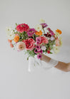 A vibrant Wylder bridal bouquet being held up against a white wall