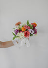A colorful Wylder bridesmaid bouquet held aloft against a white wall