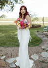 A gorgeous bride with red hair stands on a paved stone walkway holding a colorful bridal bouquet from the Wylder collection