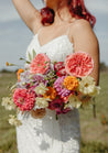 A gorgeous bride with red hair stands just out of focus holding a colorful bridal bouquet from the Wylder collection