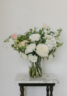 Medium Haven centerpiece with white roses and pink accents on gray marble table against a white wall