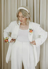 A woman in a white suit wears a Wylder corsage on her wrist and another pinned to her lapel