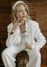 A blonde woman in a white suit wears a boutonniere on her wrist and lapel