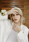 A woman in a white suit frames her face with her hands and models the Haven corsage