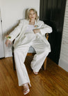 A blonde woman in a white suit slouches in a decorative chair and models the Chelle Boutonniere