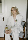 A woman in a white suit wearing a Chelle boutonniere and corsage